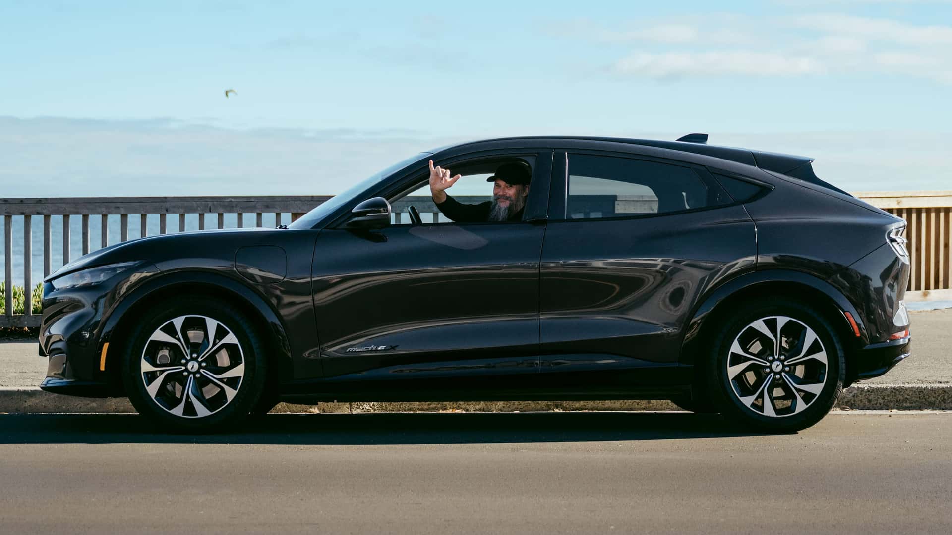 Mand kører en sort elbil langs en kyststrækning under en klar himmel