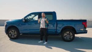 Mand ved siden af en blå elektrisk pickup truck på parkeringsplads.