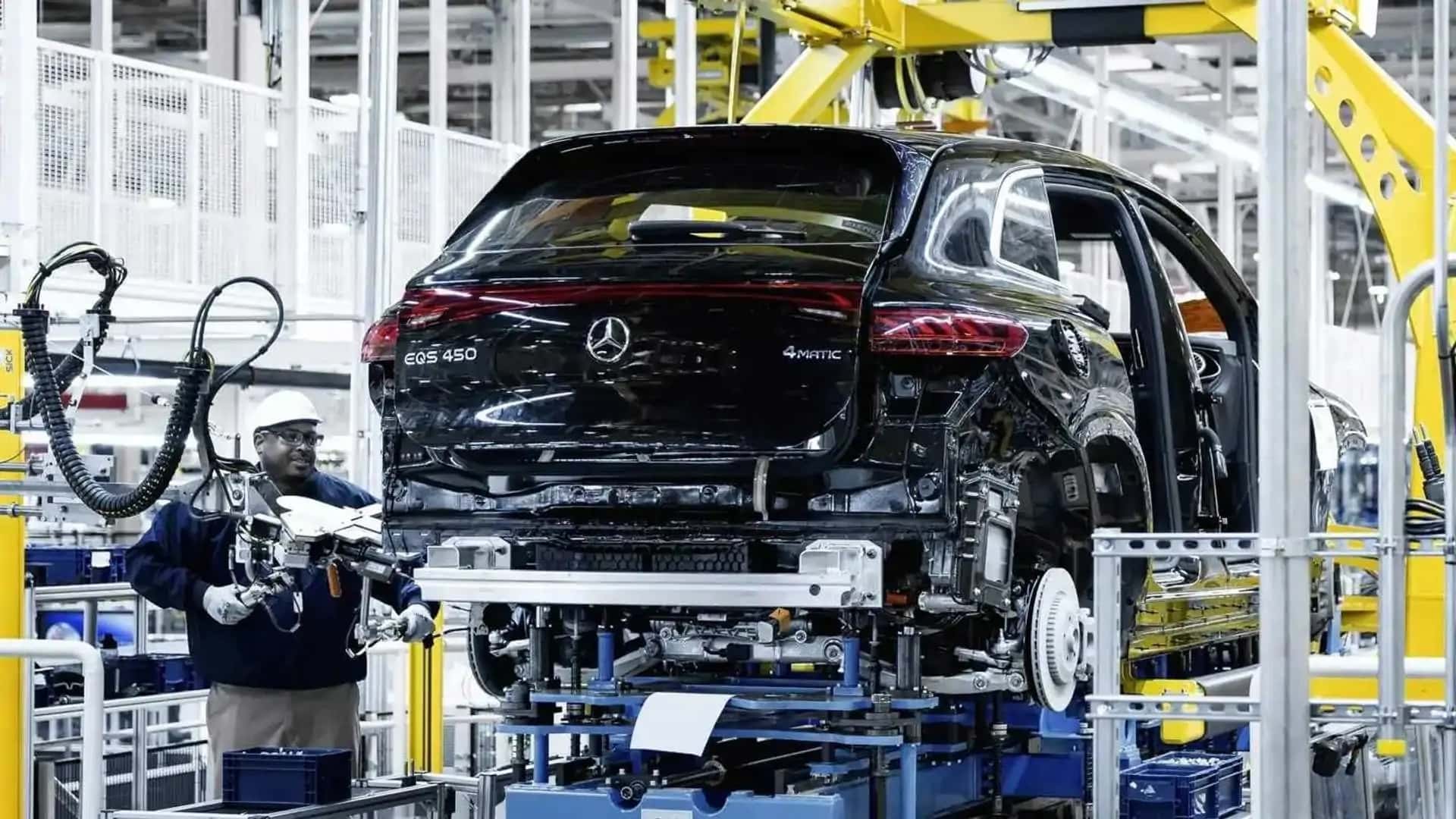 Mercedes EQS 450 under produktion på en fabrik, hvor en medarbejder inspekterer bilens montering.