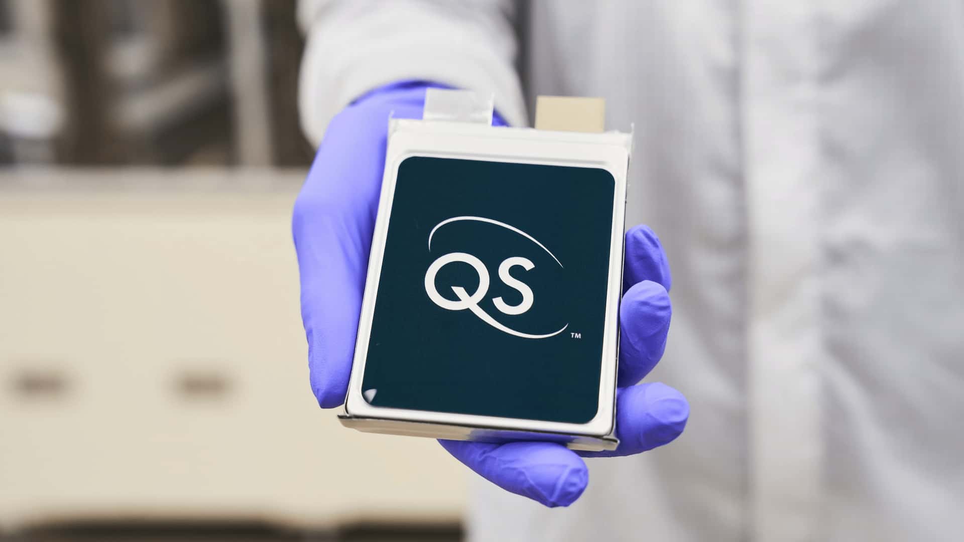 Laboratorieforsker holder QS-batteripakke iført blå handsker