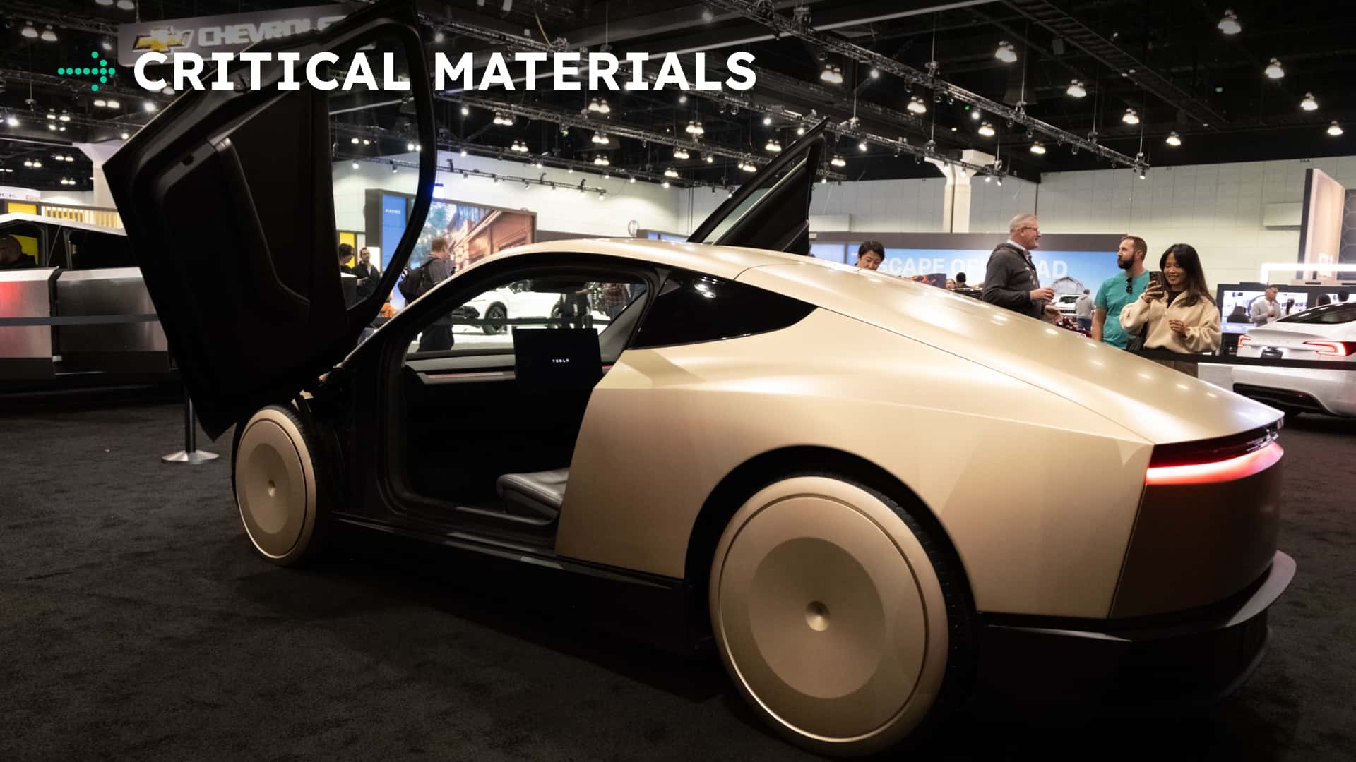 Elektrisk bil i en biludstilling med teksten 'CRITICAL MATERIALS' over bilen