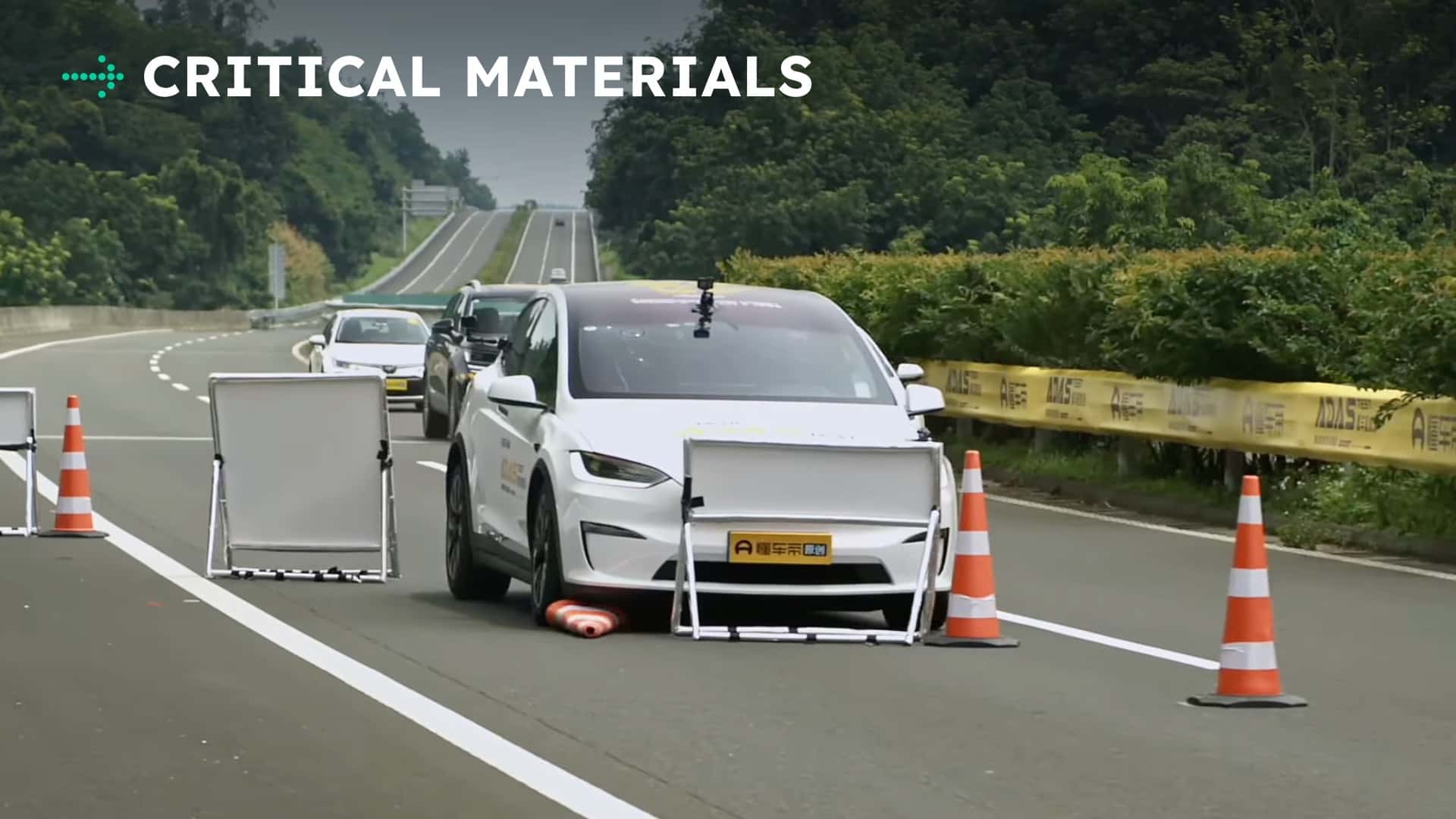 Tesla-bil under kørselstest med kritiske materialer og trafikafspærringer på vejen