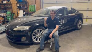 Mand sidder ved siden af en sort Tesla i en garage