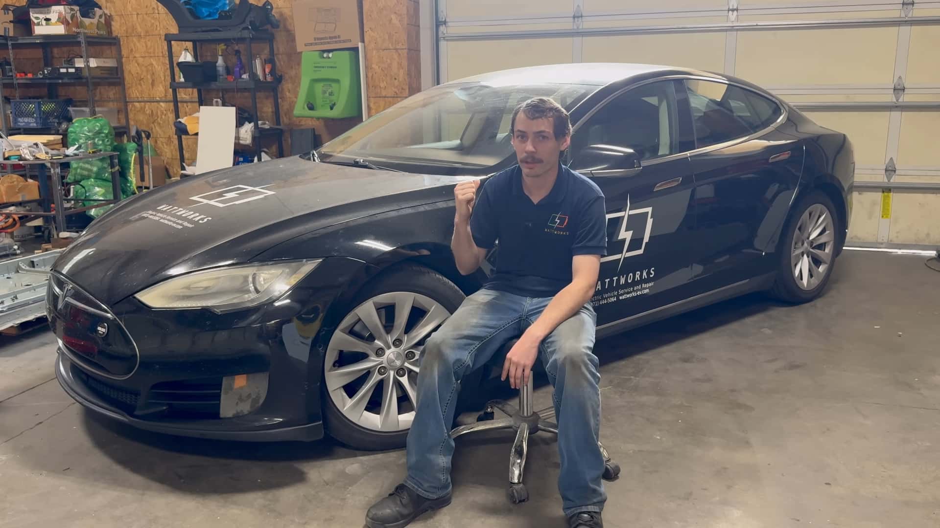 Mand sidder ved siden af en sort Tesla i en garage