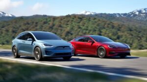 To Tesla-biler, en i blå og en i rød, kører side om side i naturskønne omgivelser.