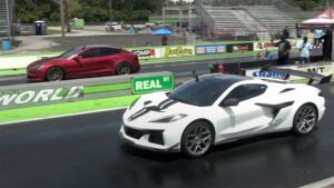 Tesla Model S i rød farve ved siden af en hvid sportsvogn på racerbanen under et kapløb.