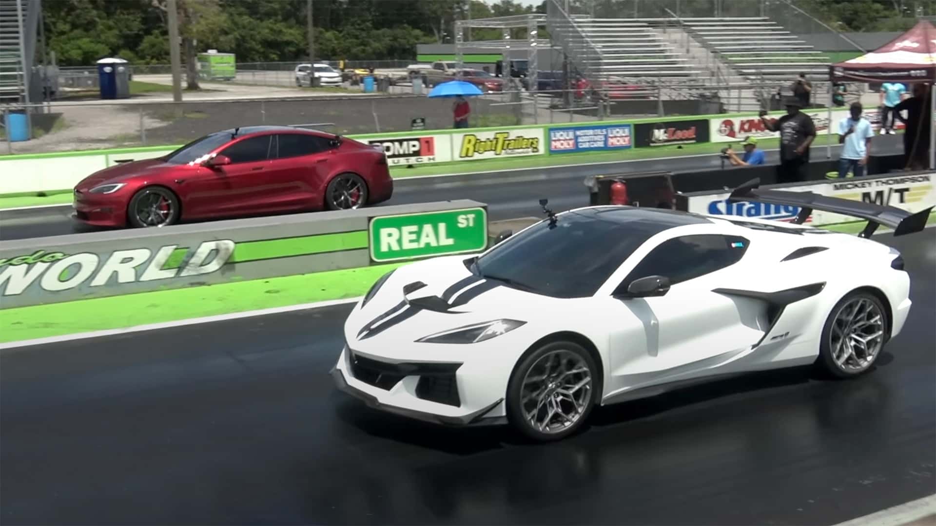 Tesla Model S i rød farve ved siden af en hvid sportsvogn på racerbanen under et kapløb.