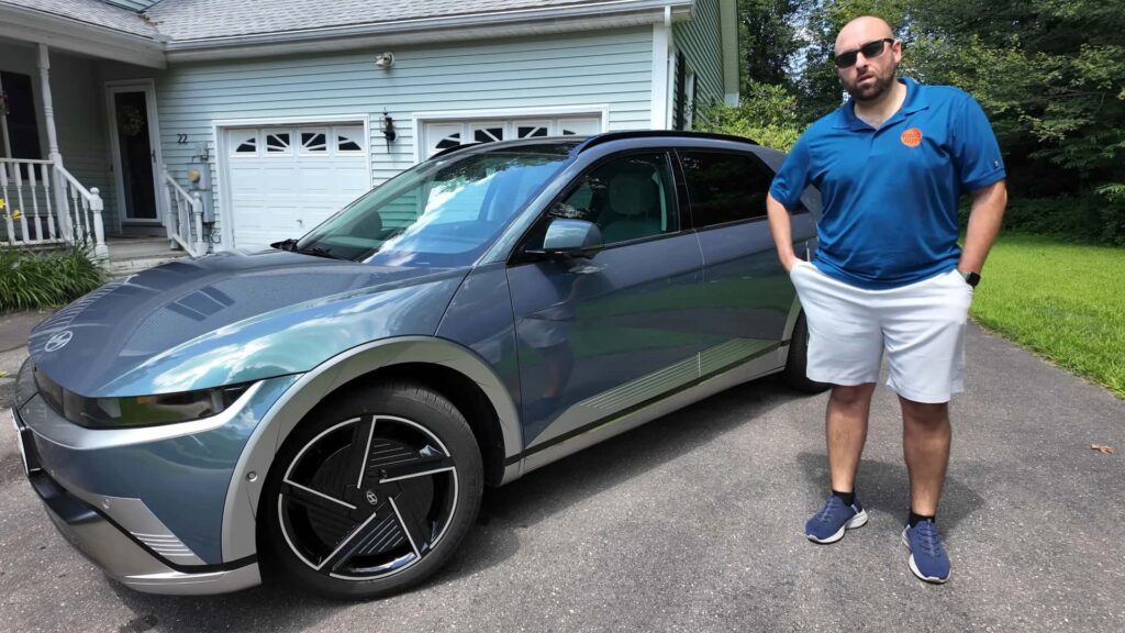 Mand står ved siden af en elektrisk bil foran et hus
