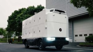 Futuristisk elektrisk lastbil kører på vej ved siden af moderne bygninger