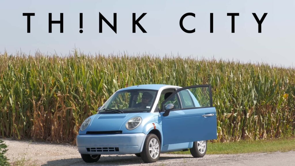 Blå Think City elbil parkeret foran en majsmark