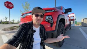 Mand i solbriller foran en rød Chevrolet pickup truck ved en Tesla ladestation