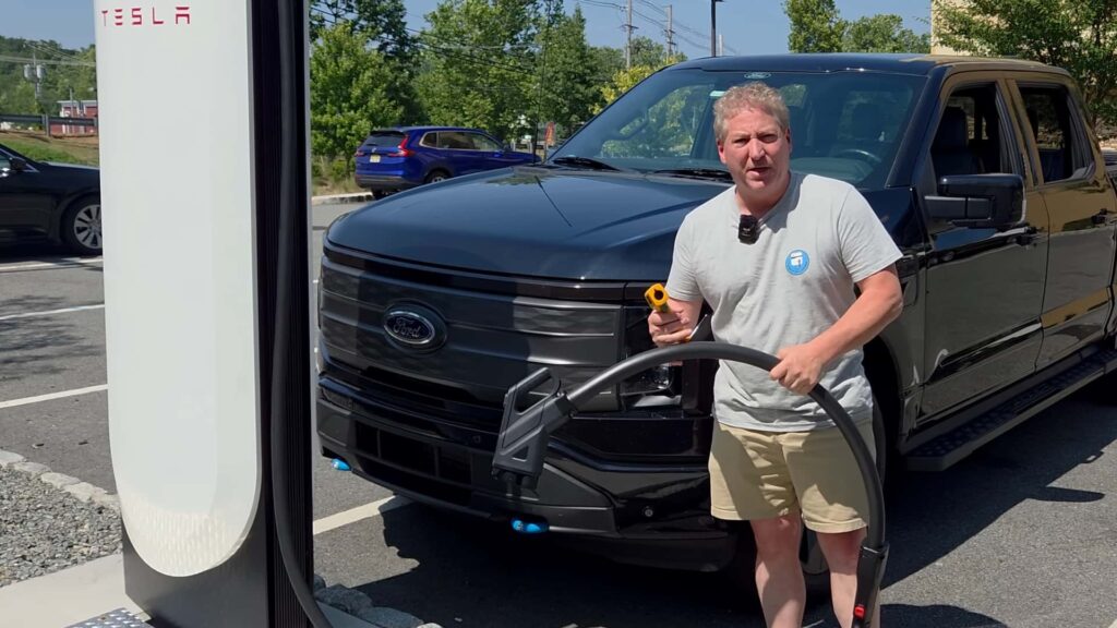 Mand ved siden af en sort elbil holder en Tesla-ladestik
