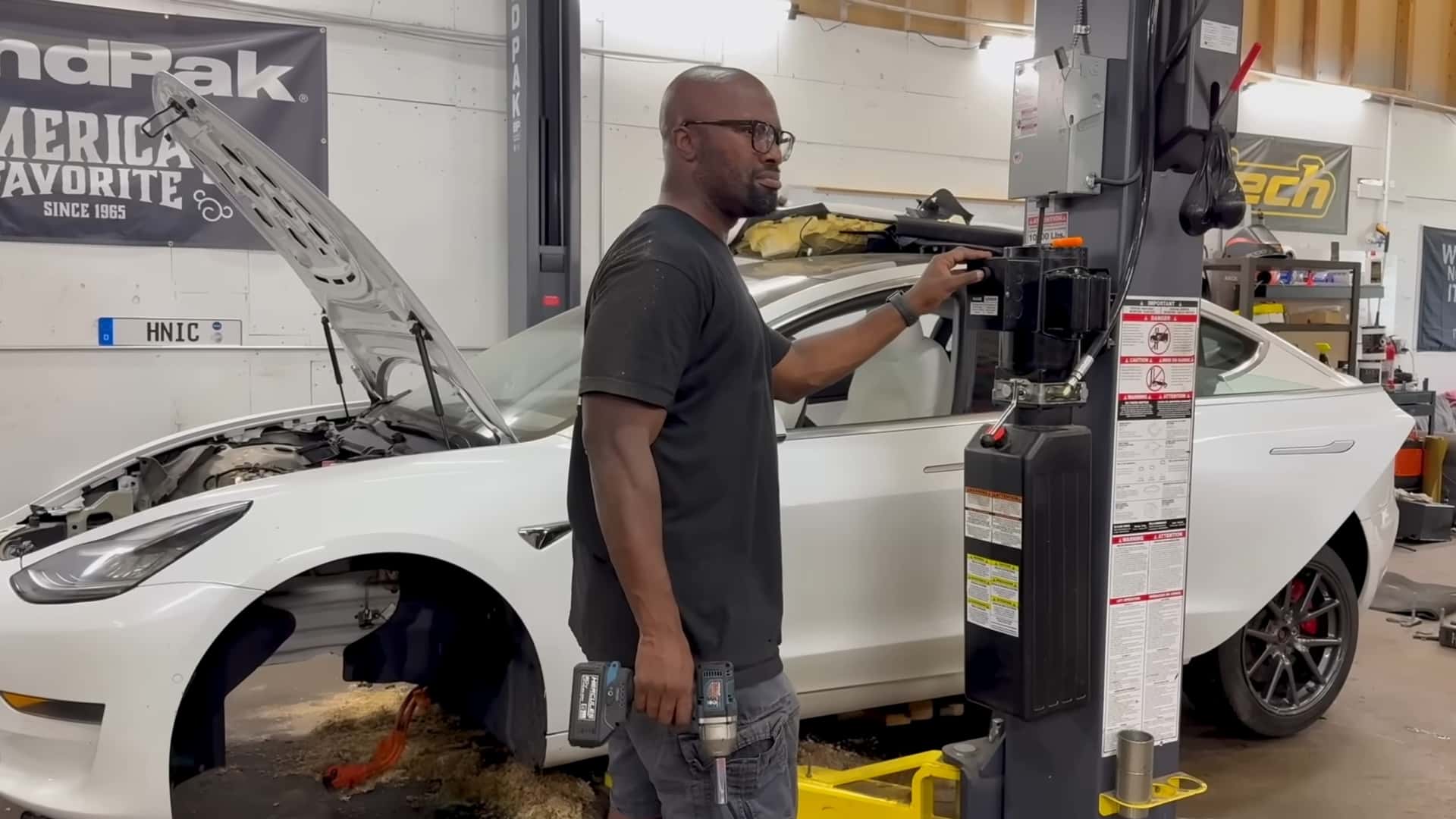 Person arbejder på en Tesla Model 3 i et værksted med åbent motorhjelm