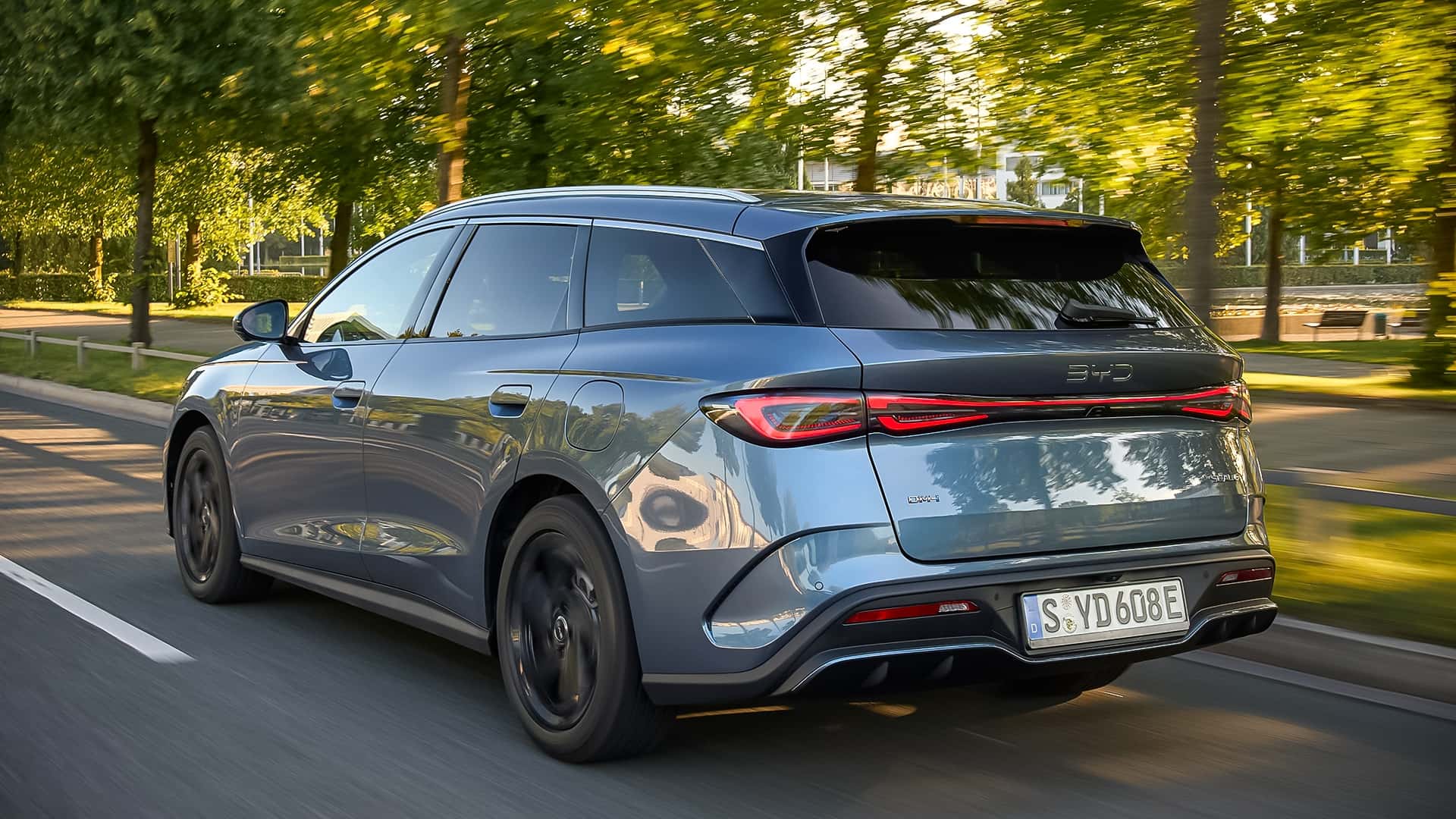 Elektrisk bil kører langs en grøn vej med træer i baggrunden