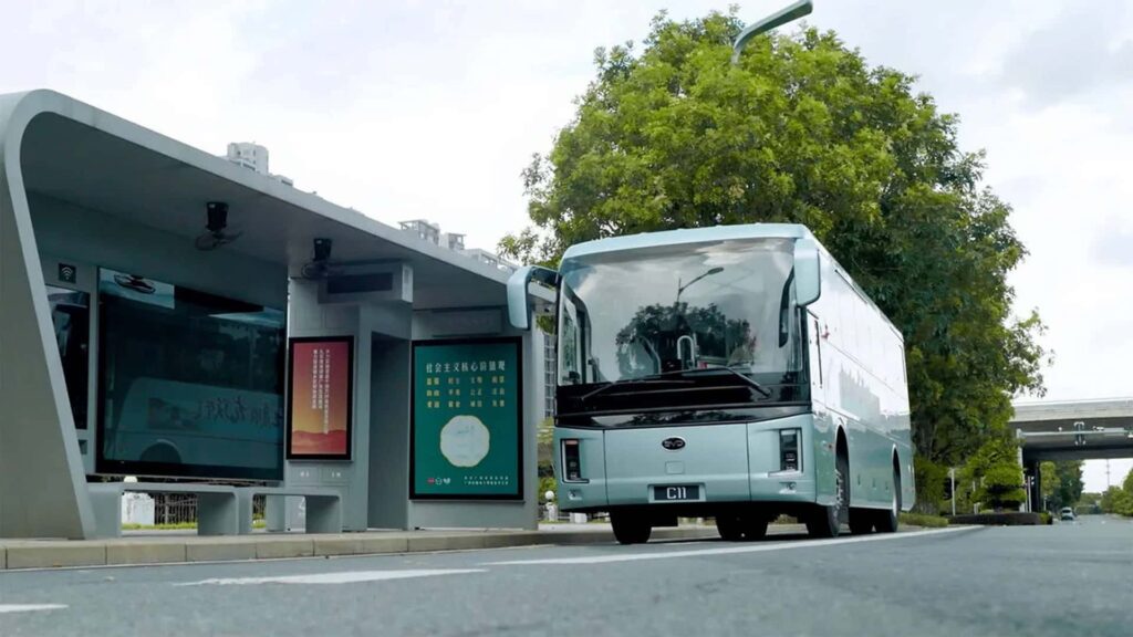 Elektrisk bus ved futuristisk busstop, omgivet af træer og moderne bygninger