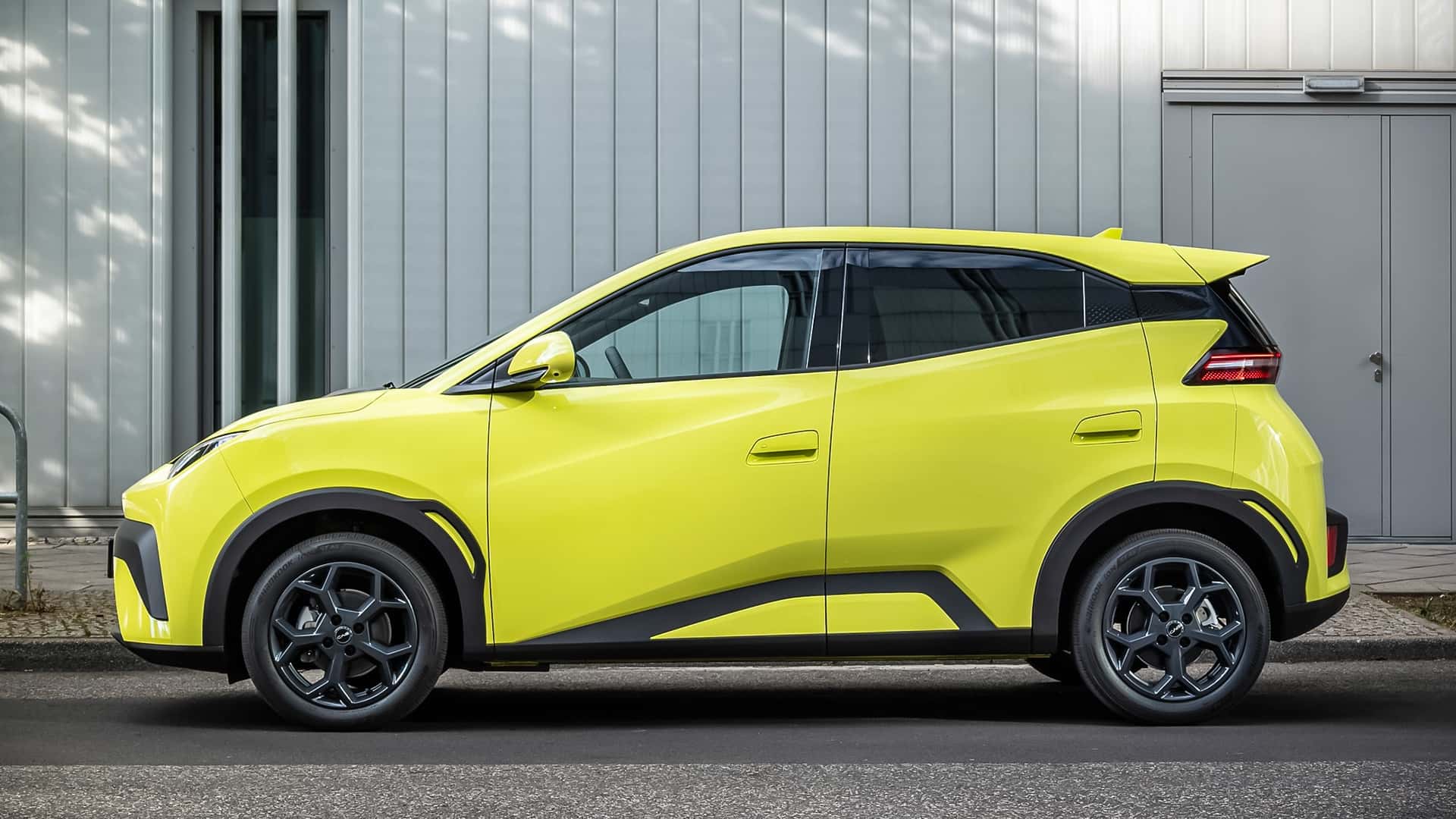 Lys gul elektrisk bil parkeret foran en industriel bygning