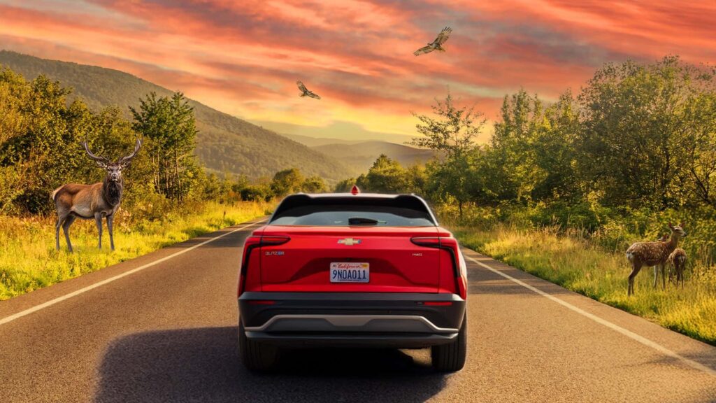 Rød elbil på vej gennem naturskøn dal ved solnedgang med hjorte og fugle i baggrunden