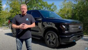 Mand står foran en sort elektrisk Ford F-150 truck udendørs på en solrig dag