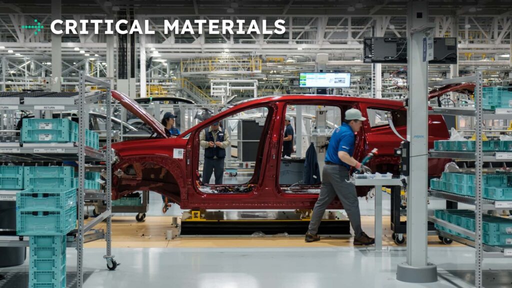 Tesla-bil under samling på fabrik, med arbejdere og kritiske materialer i nærheden