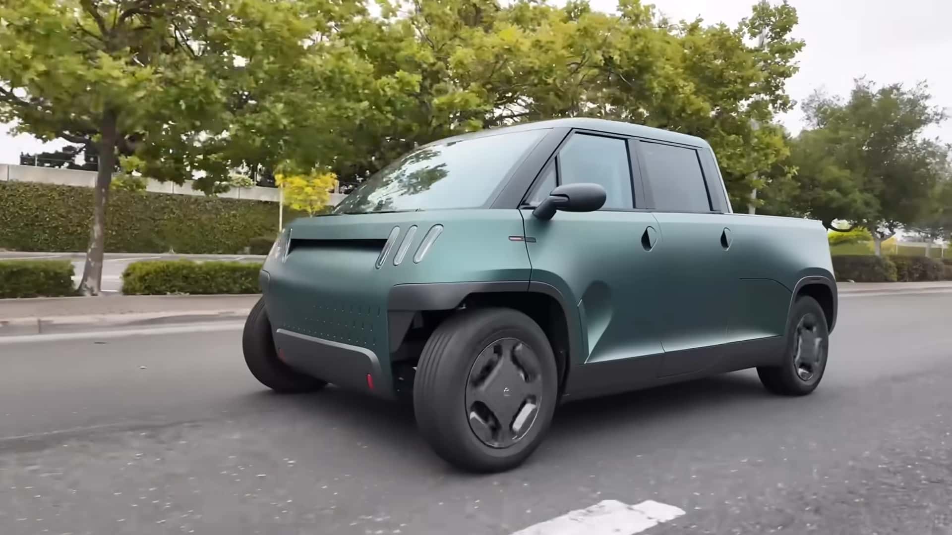 Moderne elbil med unikt design kører på vej omgivet af træer