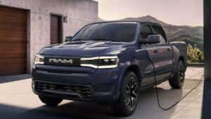 Elektrisk pickup truck fra RAM lader op foran et moderne hus med bjerge i baggrunden.