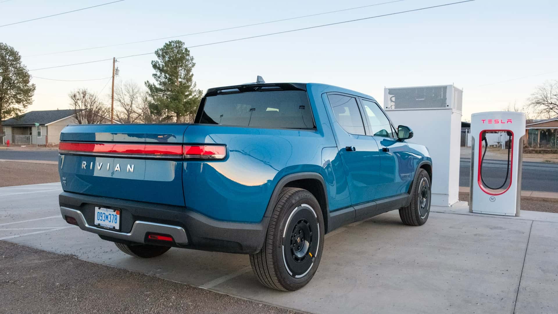 Blå Rivian pickup ved Tesla supercharger-station