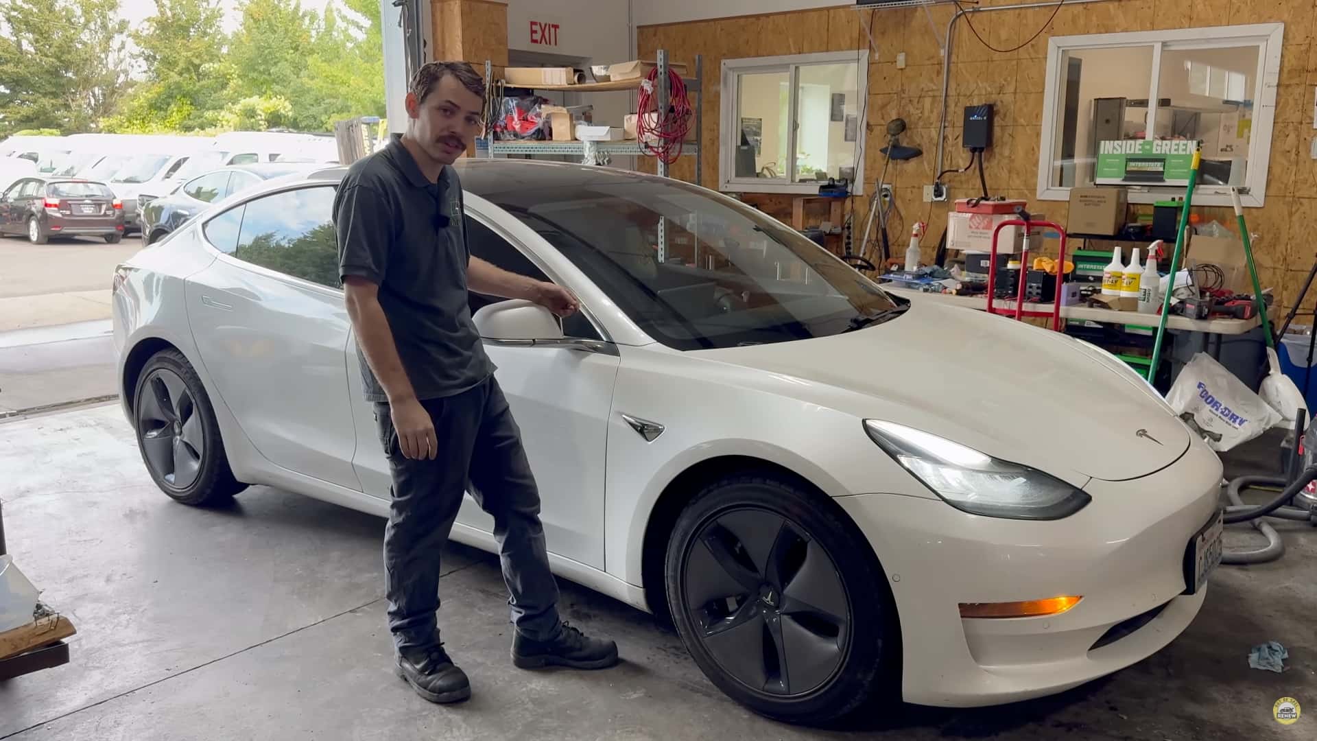 Mand ved siden af hvid Tesla Model 3 i et værksted