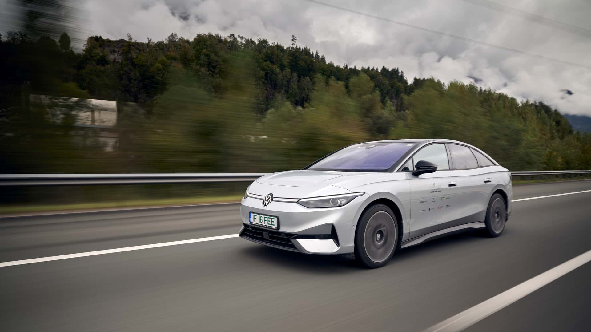 Moderne hvid elektrisk bil kører på motorvejen omgivet af natur