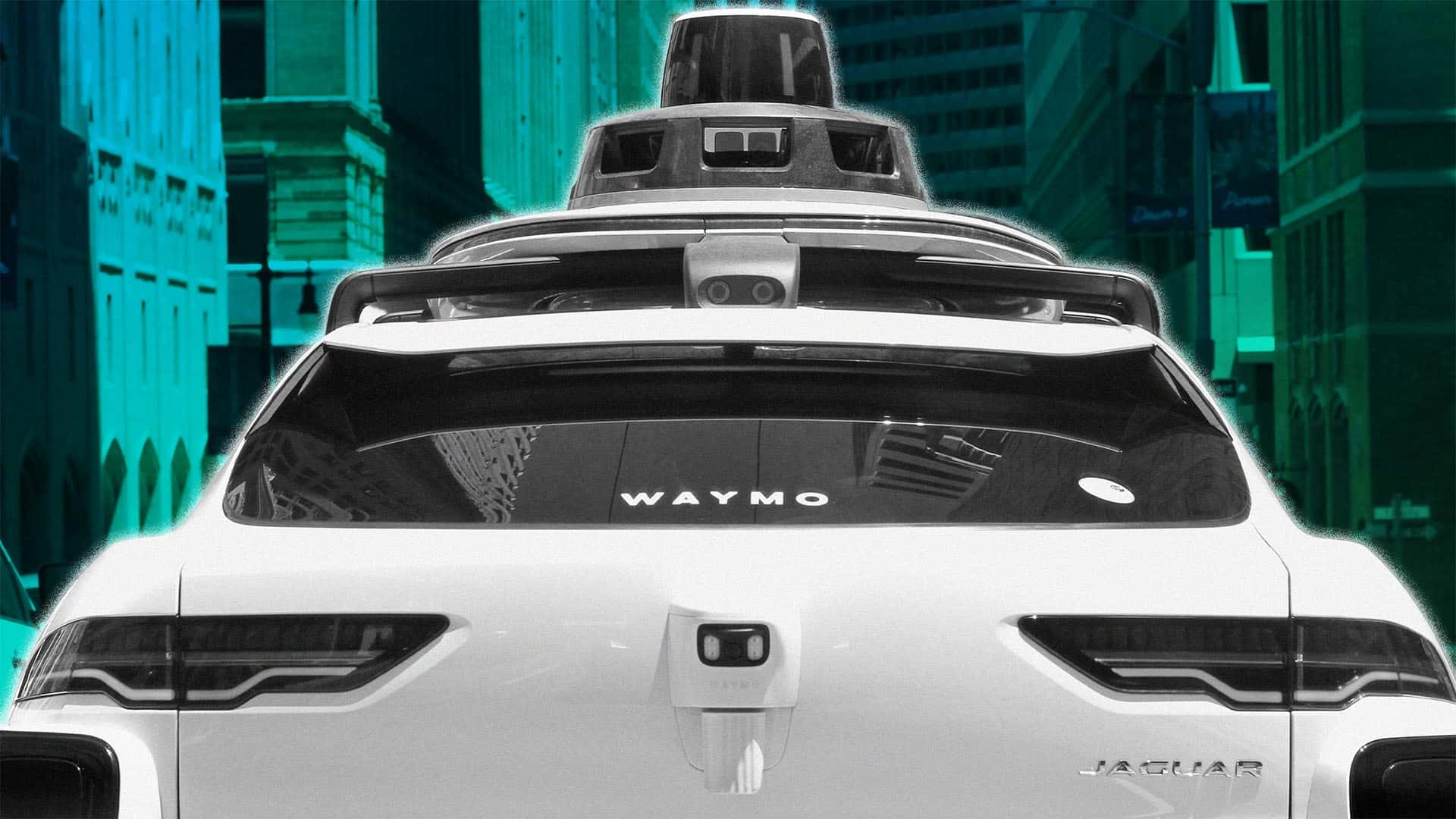 Bagenden af en hvid Jaguar med Waymo-logo, udstyret med avanceret sensorteknologi, set i en by.