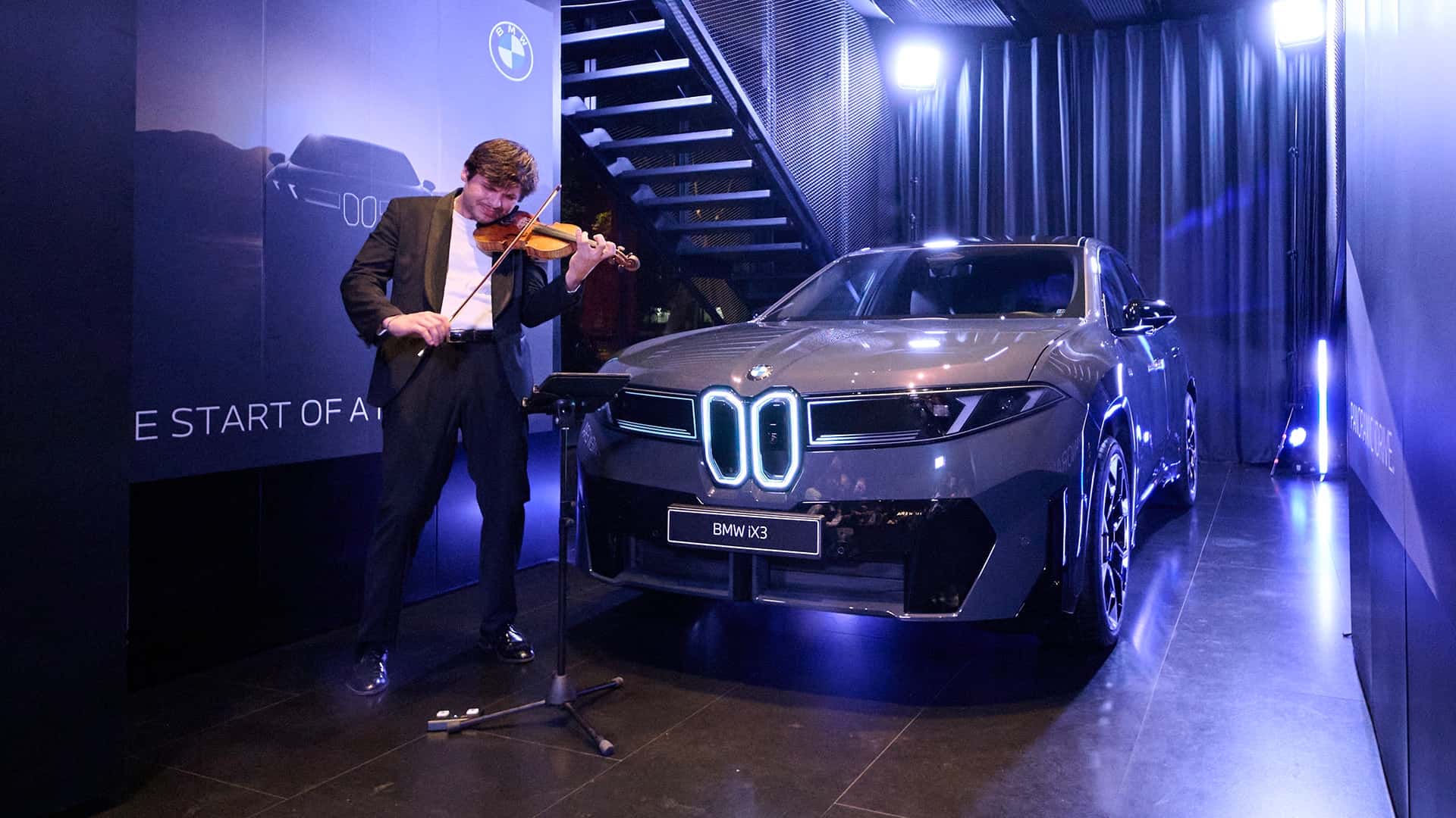 Violinist spiller ved siden af en BMW IX3 elbil i et moderne showroom