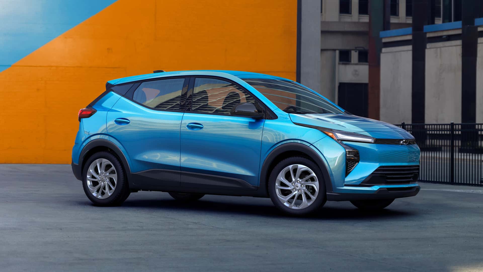 Blå elbil foran en orange væg i urbane omgivelser