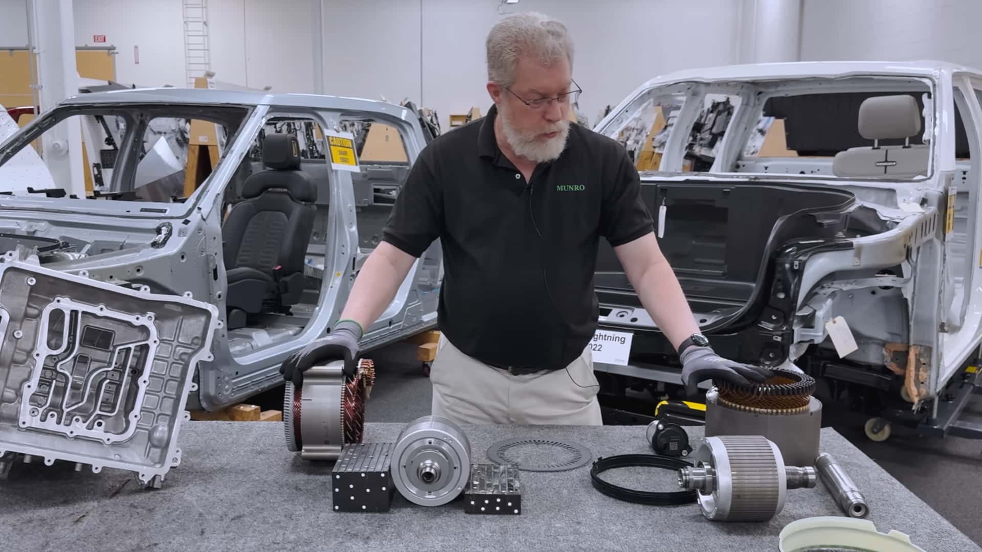 Mand undersøger elektriske bildele ved siden af Tesla bilramme på værksted