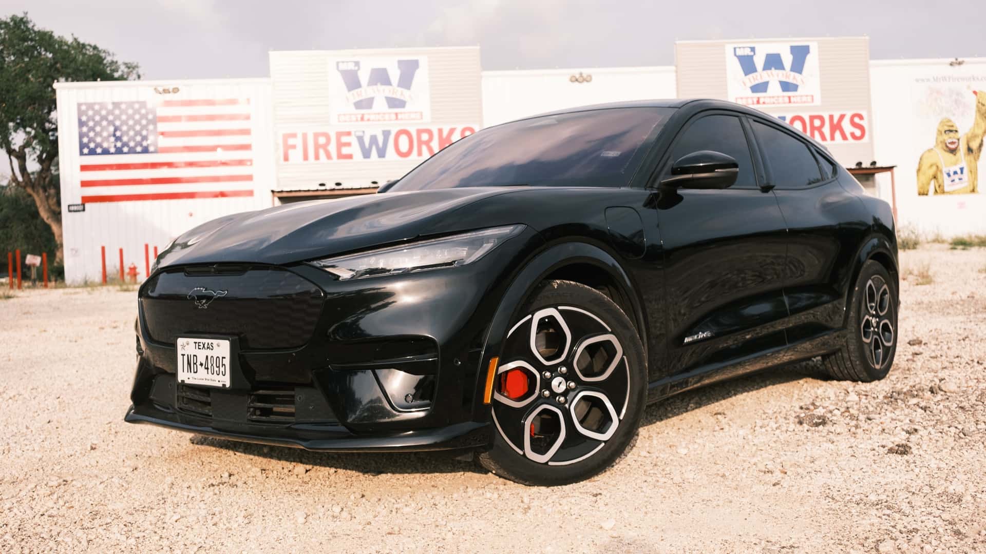 Sort elbil parkeret foran et byggemarked med amerikansk flag i baggrunden