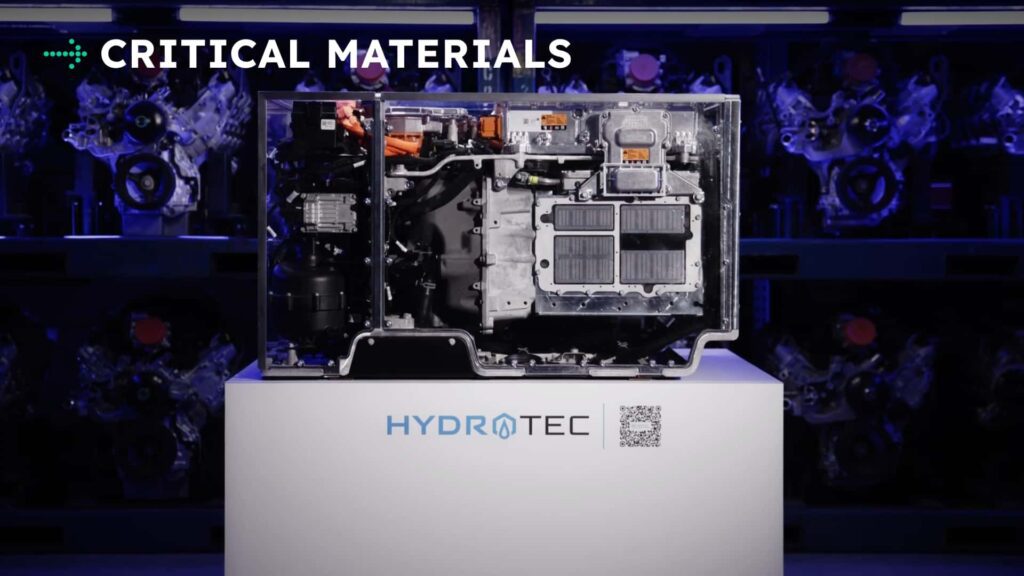 Tesla motorkomponent under glas med teksten 'Critical Materials' og logoet HYDROTEC på en hvid piedestal