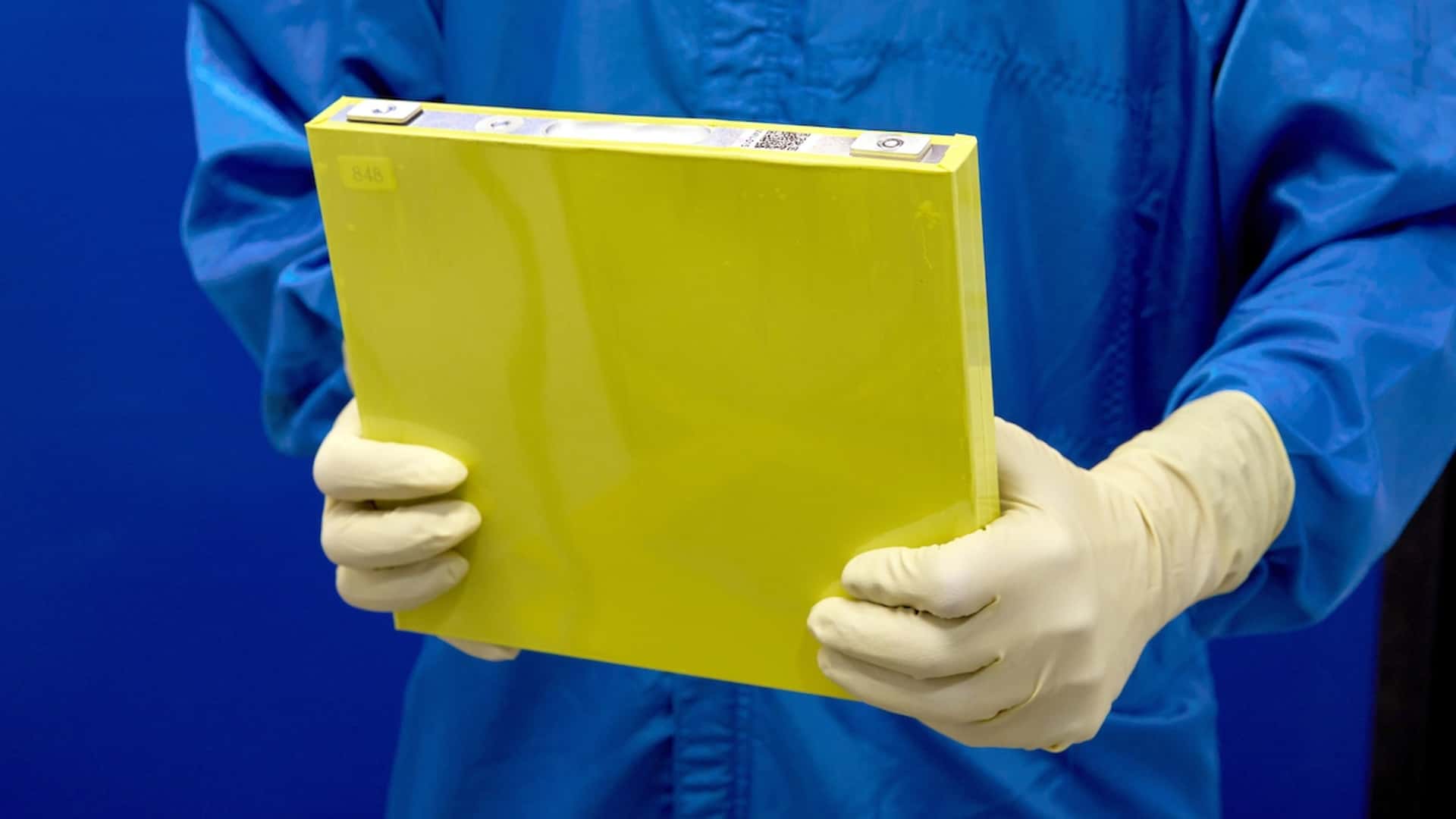 Laboratorietekniker holder en stor gul battericelle iført beskyttelsesdragt