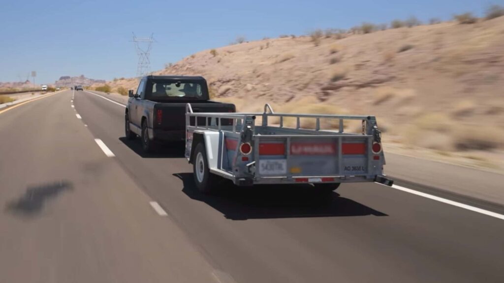 Elbil og trailer på landevej med ørkenlandskab i baggrunden