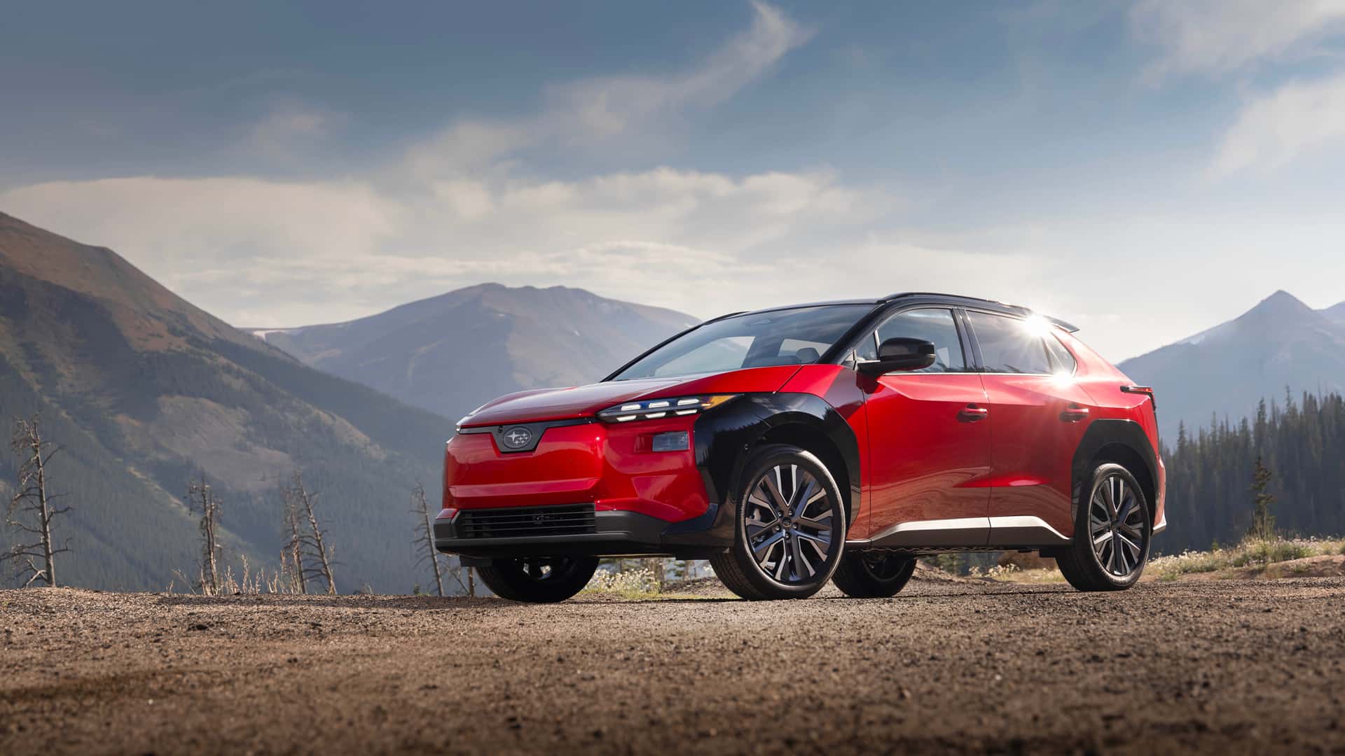 Rød elektrisk bil i bjerglandskab med blå himmel i baggrunden