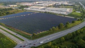 Luftfoto af stort solcelleanlæg ved Tesla-fabrik, omgivet af natur og veje