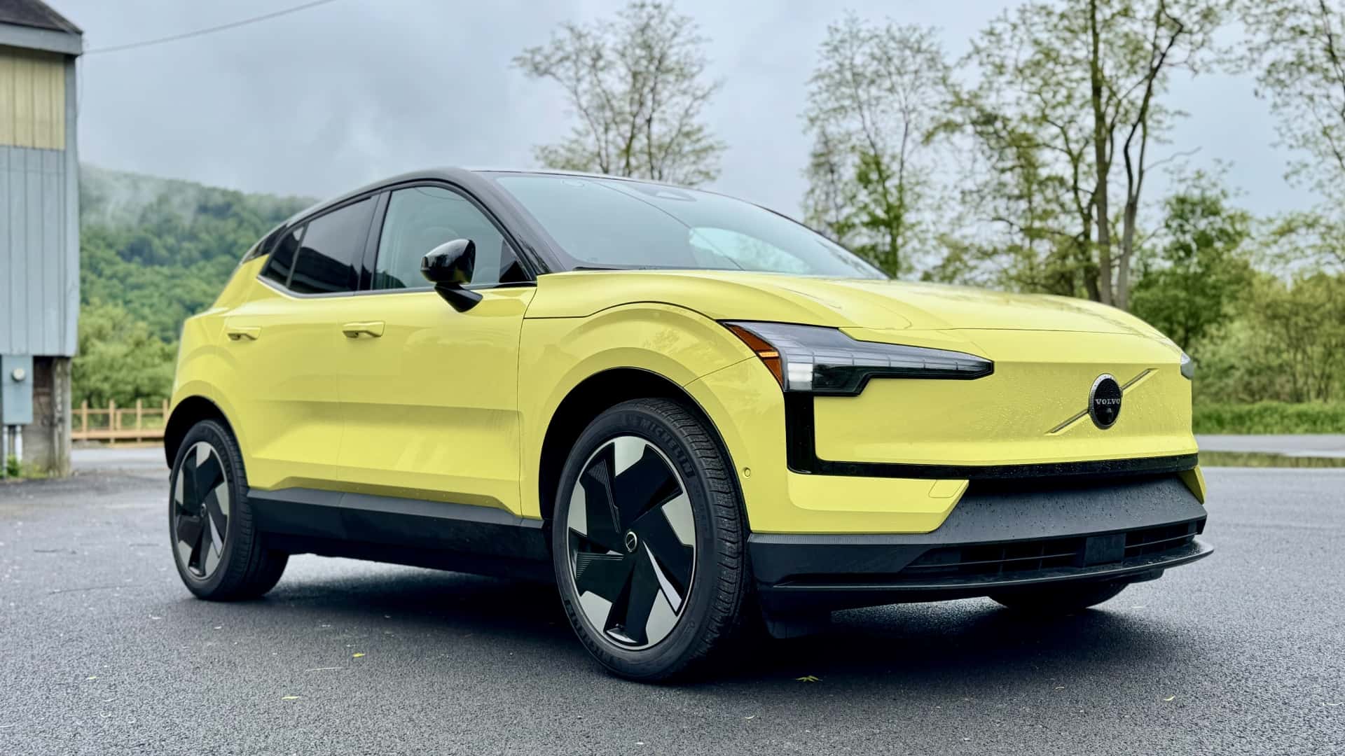 Lys gul elektrisk SUV parkeret udendørs på regnvåd vej med grønne træer i baggrunden