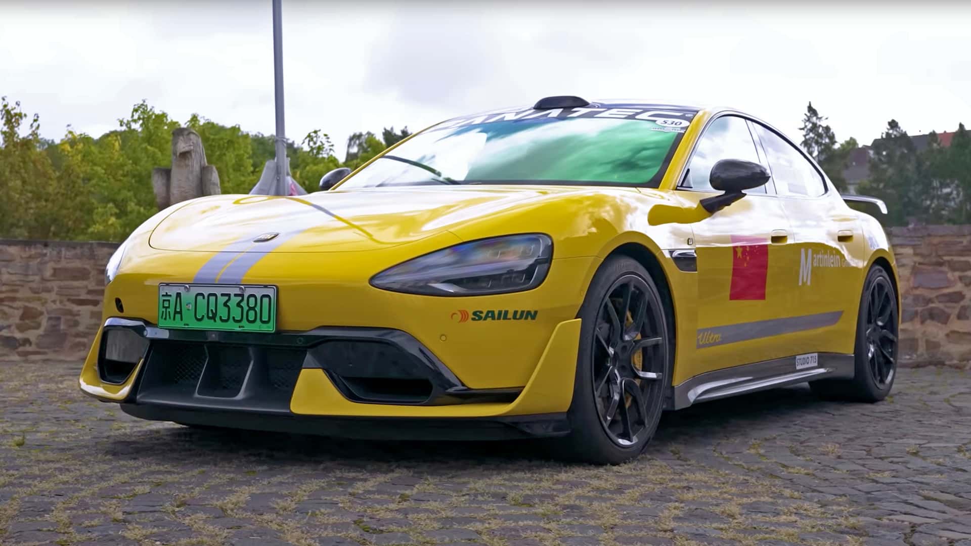 Gul elektrisk sportsbil med kinesisk nummerplade og sponsormærker, parkeret på brosten