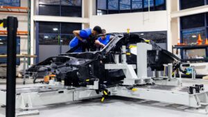To teknikere arbejder på samling af en Tesla bilramme i en moderne facilitet.