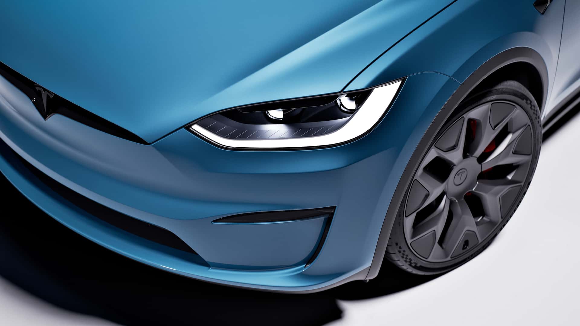 Close-up af forlygten og hjulet på en Tesla i en blå farve.