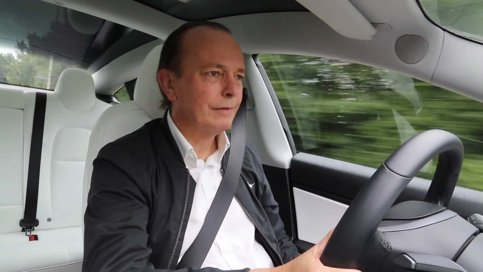 Person kører i en Tesla Model 3 med hvidt interiør på vej