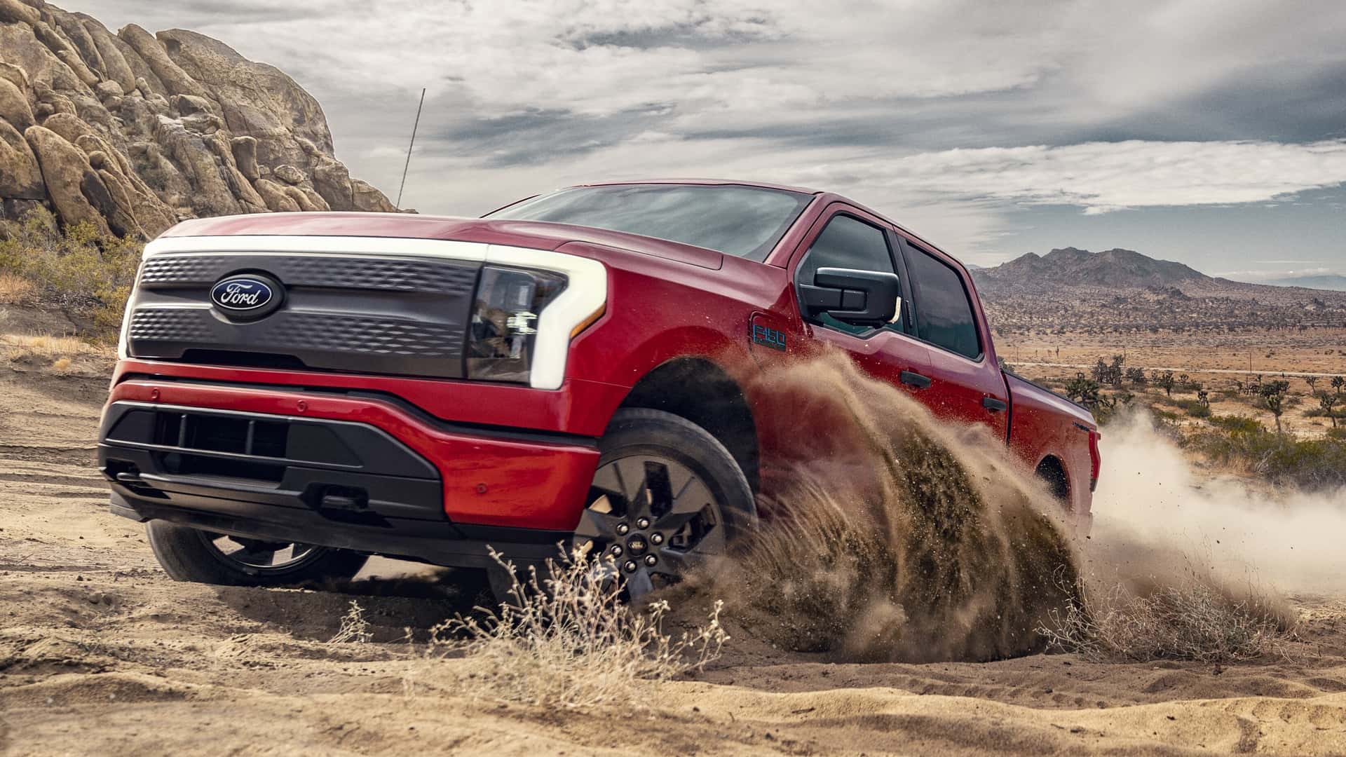 Rød elektrisk pickup-køretøj kører gennem sandet i en ørkenlandskab