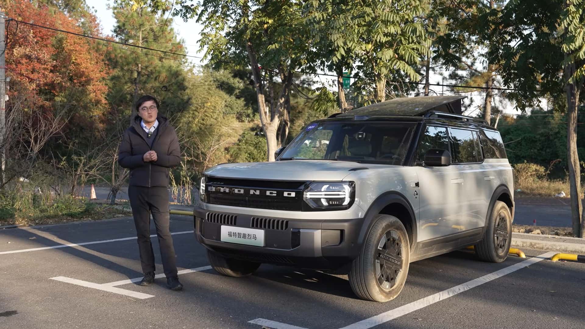 Person står ved siden af en Ford Bronco på en solrig dag omgivet af træer