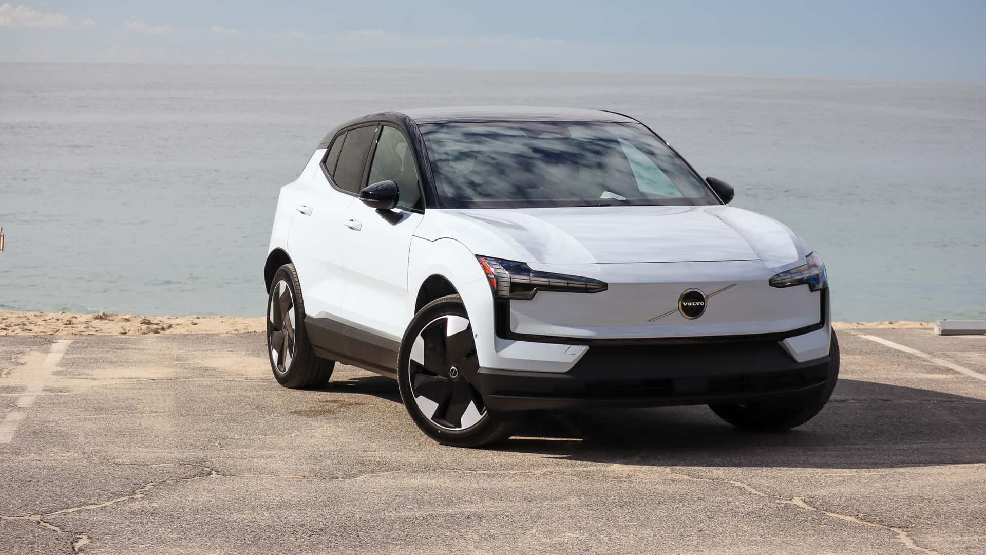 Hvid elektrisk SUV parkeret ved stranden med havudsigt