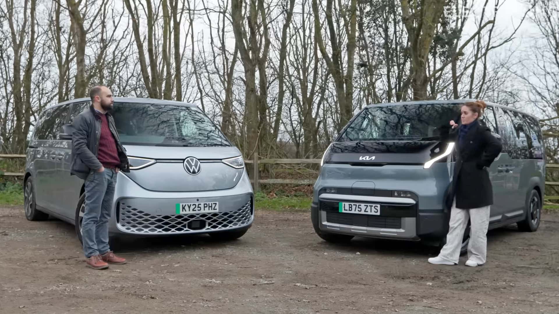 To personer diskuterer ved siden af elektriske biler fra Volkswagen og Kia, parkeret på en skovvej.