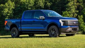 Blå elektrisk pickup truck parkeret på græsplæne med skov i baggrunden