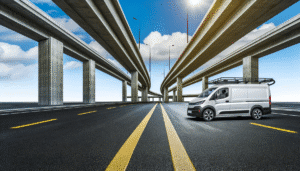 Hvid elektrisk varevogn på moderne motorvej under flere broer mod en klar blå himmel