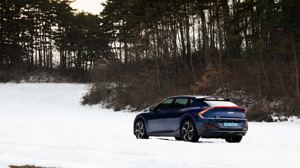 Blå elektrisk bil kører gennem snedækket landskab med skov i baggrunden